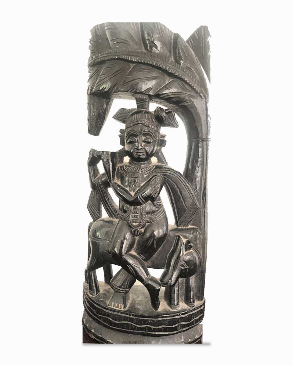 Vintage carved teak sculpture of Krishna seated on a cow beneath a tree, playing the flute