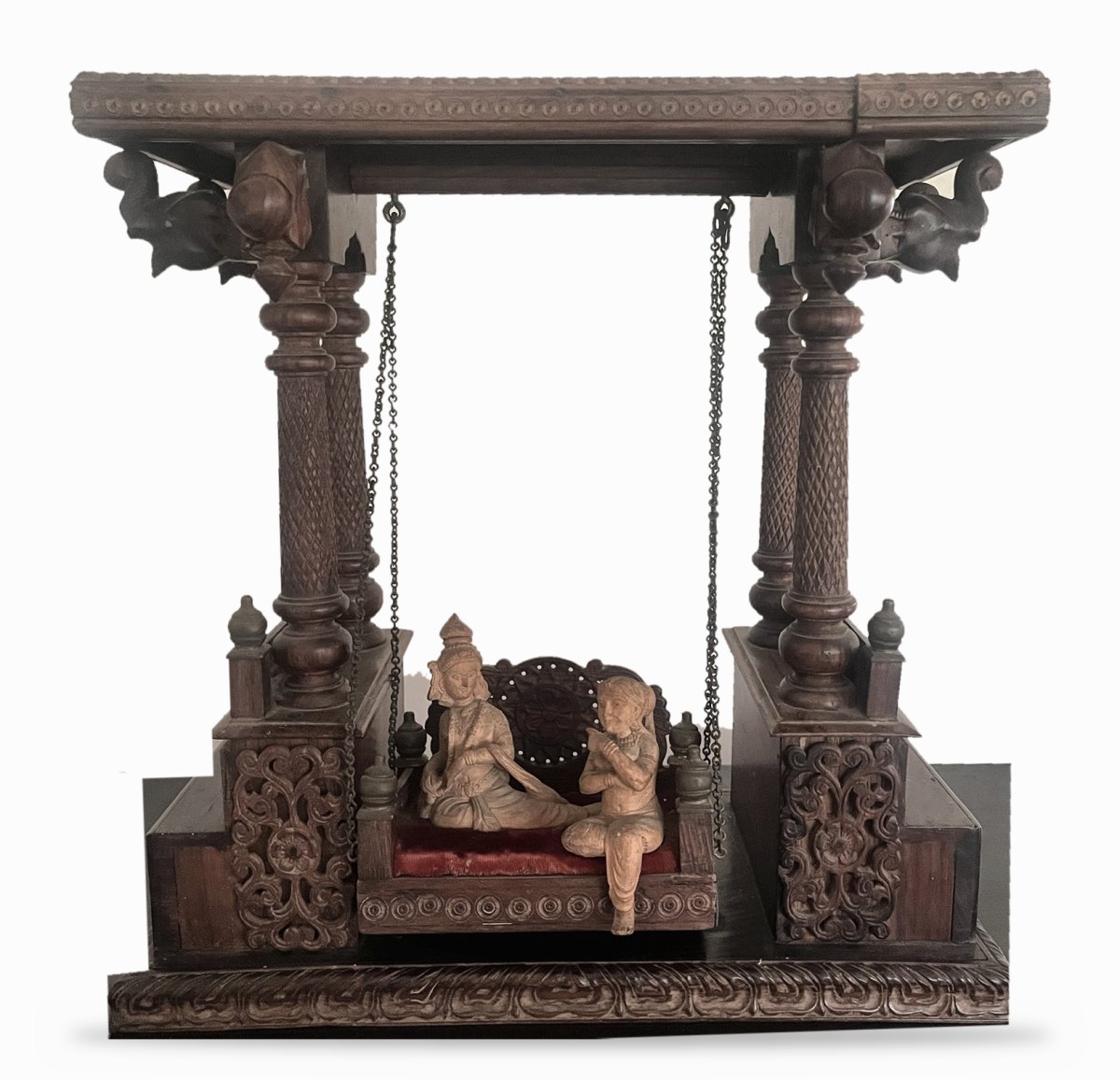 Vintage carved teak swing with Radha and Krishna seated on a red velvet seat