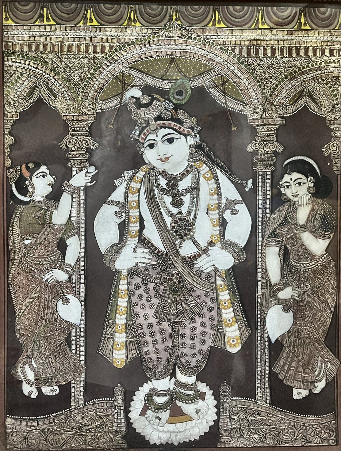 Antique Tanjore painting of Krishna on a lotus beneath jewelled arches, with two gopis, in a carved wooden frame